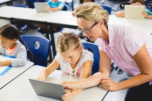 School girl and teacher using digital tablet in classroom