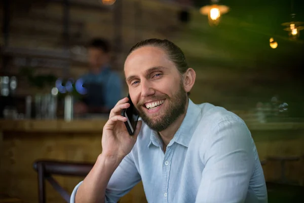 Smiling man talking on mobile phone at cafe