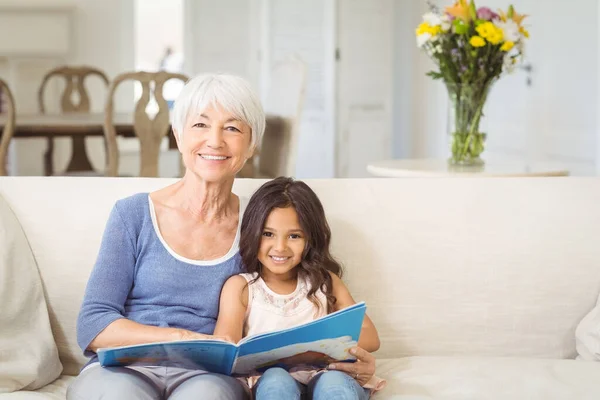 Smiling grandmother and granddaughter sitting together on sofa with photo album