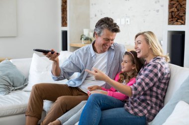 Oturma odasında patlamış mısır yerken gülümseyen aile televizyon izliyor.