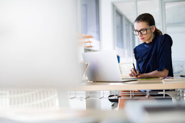 Женщина-руководитель работает за ноутбуком и графическим планшетом за своим столом