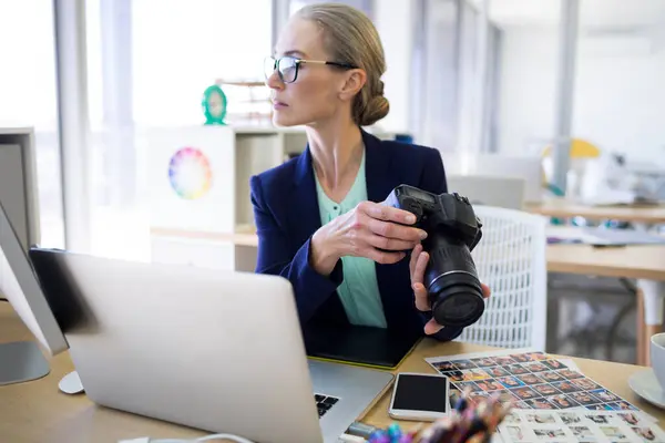 Female executive holding digital camera at her desk