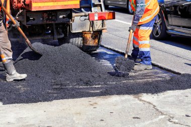Çalışan ekip, yolun tamir alanında sıcak asfaltı küreklerle el ile eşit olarak dağıtır..