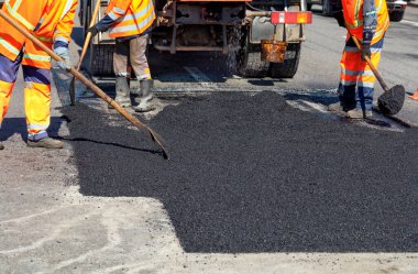Çalışma ekibi yol tamir ederken elle kürek ile sıcak asfalt pürüzsüzler.