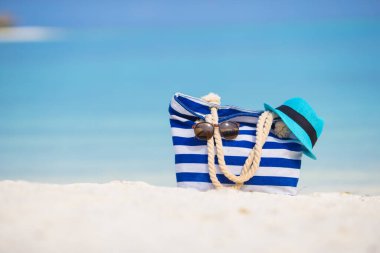 Plaj aksesuarları - mavi çanta, hasır şapka, güneş gözlüğü beyaz plaj üzerinde