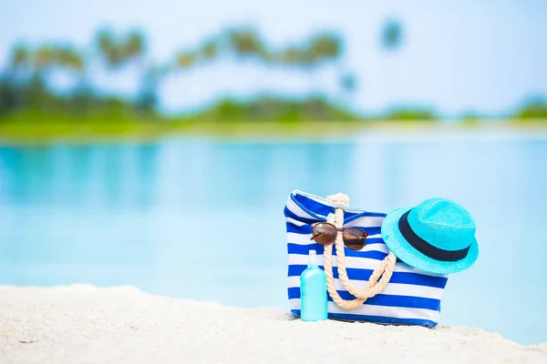 蓝色的袋子 稻草帽子 墨镜和防晒霜瓶在白色的沙滩上 — 图库照片