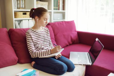  Liseli kız evde dizüstü bilgisayarla ödevini yapıyor. Çocuk çalışmak için aletler kullanıyor. Çevrimiçi eğitim ve çocuklar için uzaktan öğrenme. Karantina sırasında evde eğitim 