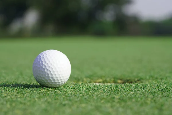 穴の近くの緑の草の上のゴルフボールのクローズアップ — ストック写真