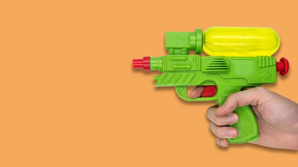 Hand holding gun water toy on orange background. Free space for text
