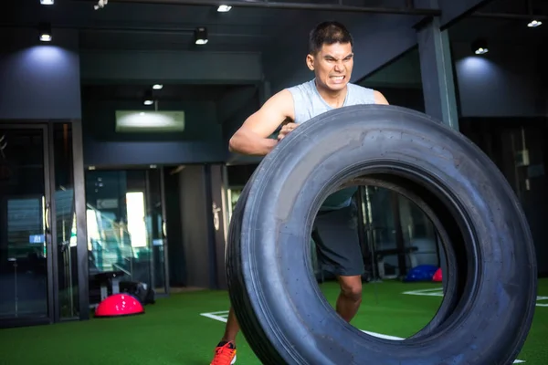 Strong muscular man lifts tire as part of his fitness program.