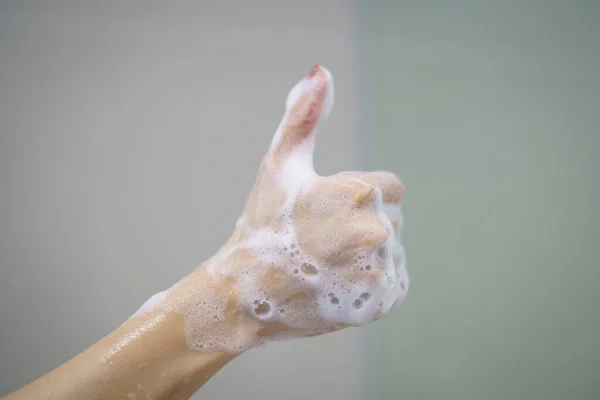 石鹸からの柔らかい泡が付いている手は親指を示しています — ストック写真