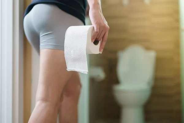 トイレの前でトイレットペーパーロールを保持している男性の比重ビュー — ストック写真