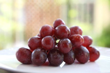 Beyaz masadaki cam kasede taze kırmızı üzümlerin görüntüsünü kapat.