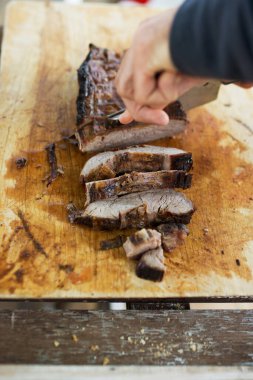 Ahşap tahtada ızgara et dilimleyen bir adam.