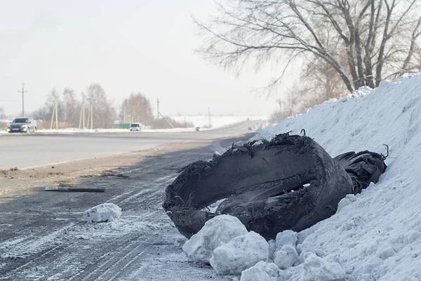 トラックから引き裂かれた車のタイヤは道路の側面の雪の中にあります — ストック写真