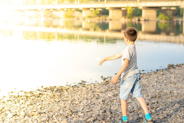 a child, a teenager, on a stony shore throws stones into the river