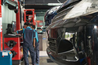 Araba süspansiyonları ve arka plandaki işçiler kontrol ediliyor