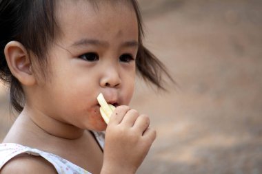 Asyalı küçük kız bahçede patates cipsi yiyor..