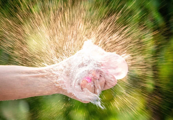 手の近くに水を入れ 庭のぼやけた自然の背景にそれを飛び散らせる風船を絞る — ストック写真