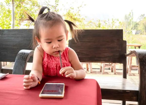 Азиатская Маленькая Девочка Сидит Деревянном Стуле Глядя Смартфон Парке Ожидая — стоковое фото