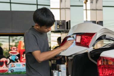 Asain adam arabayı temizliyor.