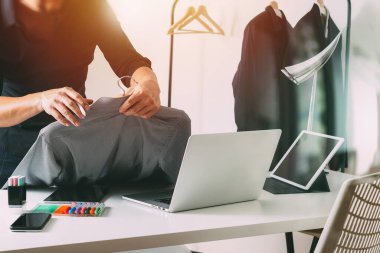 Moda tasarımcısı tişört tutuyor ve laptop kullanıyor