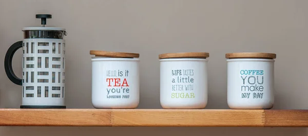 tea and coffee storage jars and a coffee plunger on a wooden shelf