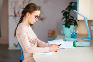 Sınıfta çalışan, cep telefonu olan ve ders çalışan güzel bir kız öğrenci. Karantina sırasında uzaktan eğitim ve öğrenme kavramı