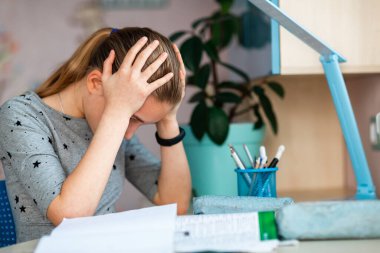 Ders notları, cep telefonları ve derslerle evde çalışan stresli ve yorgun bir genç kız. Karantina sırasında uzaktan eğitim ve öğrenme kavramı