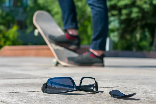 Lost black glasses lie on the road against the background of a man skating on a skateboard