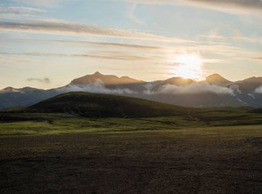 Alftavatn kamp alanında gün doğumu, karla kaplı dağlar ve yeşil tepeler. İzlanda 'nın dağlık bölgelerindeki Fjallabak Doğa Koruma Alanı' nın manzarası