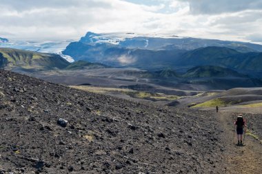 İzlanda lav çölü manzarası Tindffjallajokull buzulu ve Laugavegur yürüyüş parkurunda iki yürüyüşçü. Fjallabak Doğa Koruma Alanı, İzlanda. Yaz masmavi gökyüzü, bulutlar.