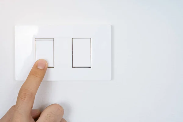 Close up finger turn on or off on white light switch with white wall at home. Power and energy saving. Copy space for text.
