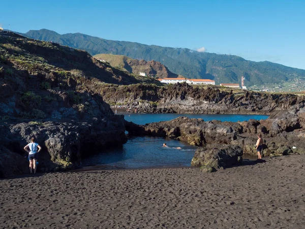 溶岩の岩崖ラグーンと暗い砂のビーチは カナリア諸島のラ パルマにあるロス カンカホスの村で観光客を実現します 青空の背景 — ストック写真