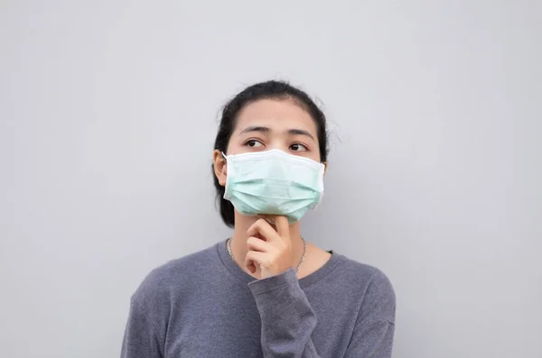 灰色の壁に立っている間若いアジアの女性は 医療面マスクを身に着けて — ストック写真