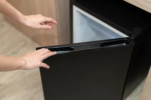 Woman hand opening refrigerator door on wooden floor.
