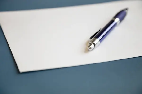 濃い青の背景の上に白い紙の上に金属ペン — ストック写真