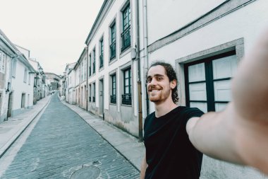 Gözlüklü genç adam eski bir İspanyol caddesinde selfie çekiyor.