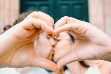Young couple making a heart symbol with the hand and kissing each other on the background