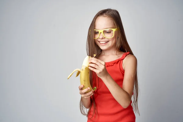 Kleines Mädchen Brille Und Rotem Kleid Mit Einer Banane Den — Stockfoto
