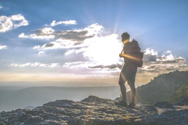 Gün batımında sırt çantalı bir adam uçurumun kenarında duruyor.