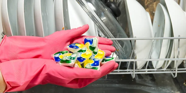 Dishwasher Detergents in hands. hands in pink gloves holds dishwasher gel capsules. Capsule for the dishwasher. Brilliant cleanliness.