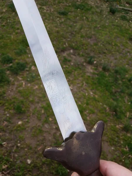 hand holding metal Chinese sword with copper handle