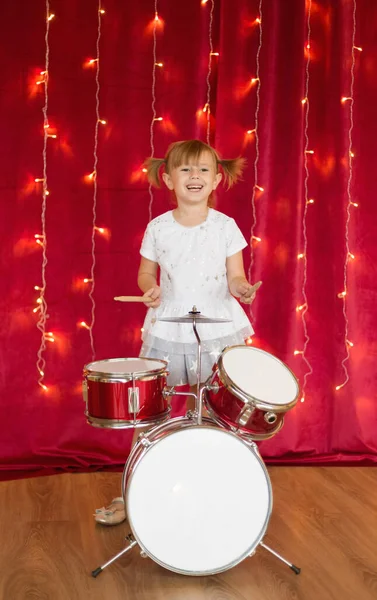 Malá Usměvavá Dívka Hraje Bubny Červeném Pozadí Novoroční Věnce — Stock fotografie