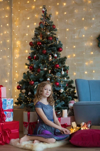 小さな子供が庭のクリスマスツリーの前に座っている — ストック写真