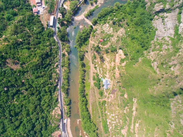 Aerial view of small river running in the forest next to mountain