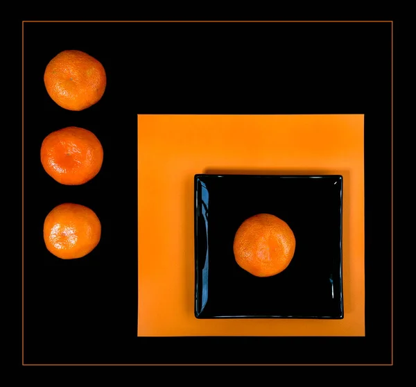 オレンジ色のテーブルの上にオレンジみかんと黒の正方形のプレートの構成 — ストック写真