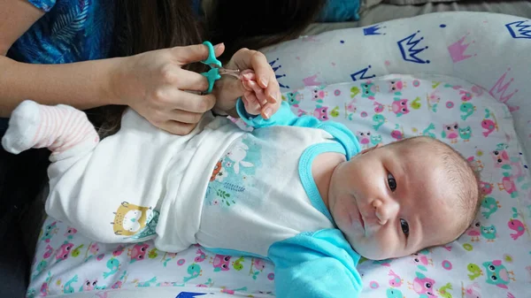 A newborn child's nails are cut with scissors