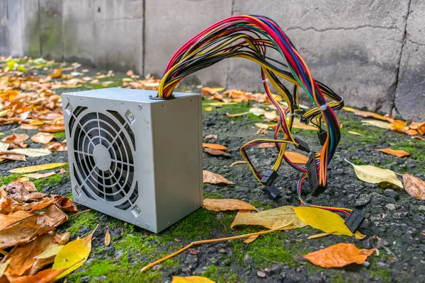 Computer power supply lying outdoors in autumn foliage at landfill