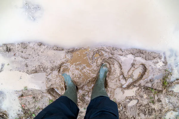 stock image feet in green rubber boots stands in wet brown mud puddle directly above view